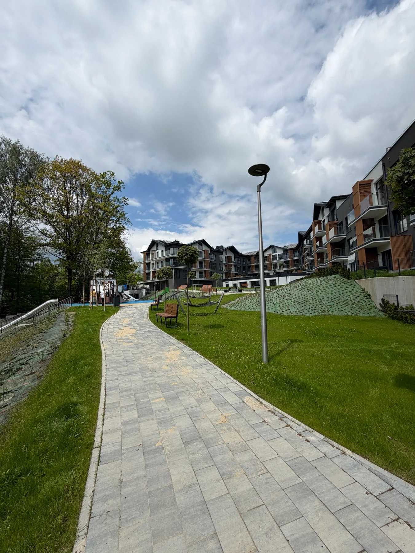 Laguna Beskidów — dlážděná cesta podél zeleně a apartmánových domů v areálu
